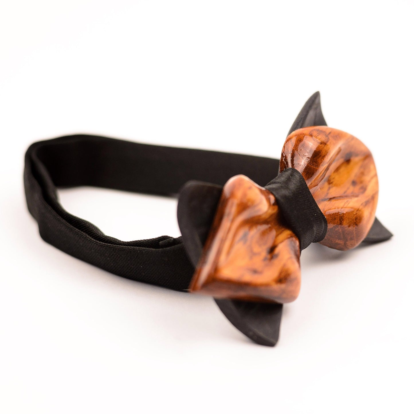 A wooden bow tie with a brown and orange wood grain pattern. The bow tie is attached to a black adjustable strap.