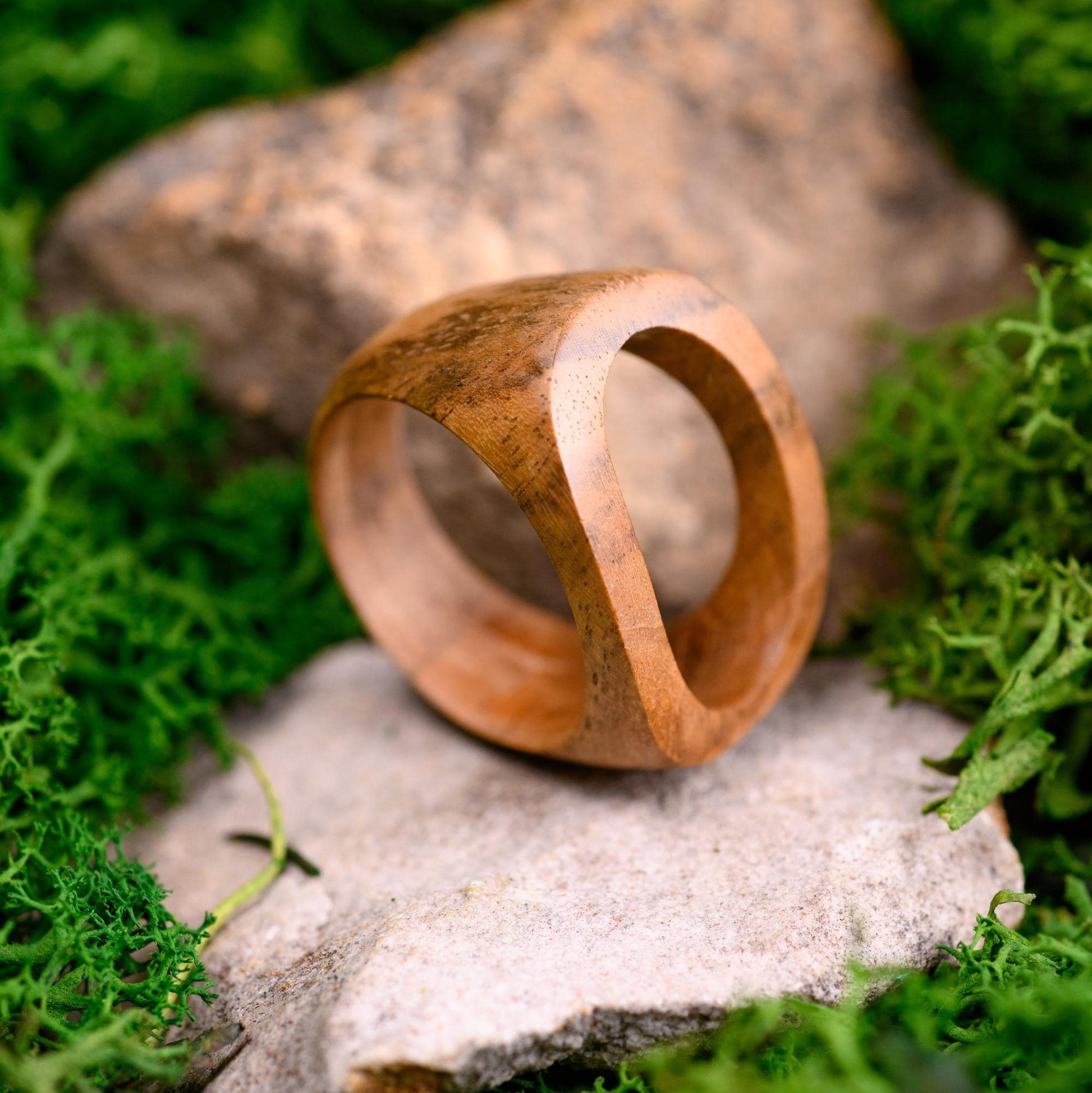 Handmade walnut wood ring with a smooth finish, displayed on a stone surface.