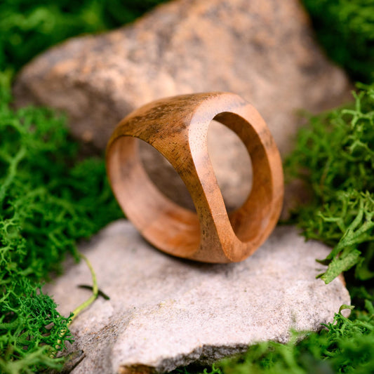 Handmade walnut wood ring with a smooth finish, displayed on a stone surface.